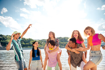 Young friends having fun outdoors at the riverside on a bright summer day, enjoying togetherness...