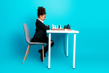 Young schoolgirl in formal attire playing a chess game against teal background, symbolizing education, strategy