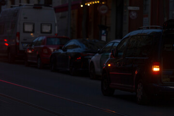 A captivating nighttime scene showcasing a bustling city street that is beautifully lined with numerous parked cars, while illuminated buildings create a vibrant backdrop in the background