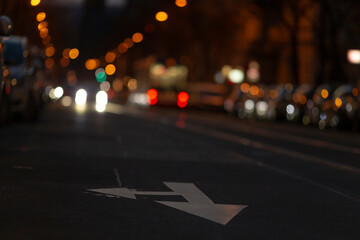 In a dimly lit street setting, there is a prominent leftturn arrow marked on the asphalt, cars...