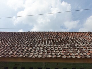 Close-up view of an old, weathered terracotta tiled roof under a bright sky with soft clouds and power lines.