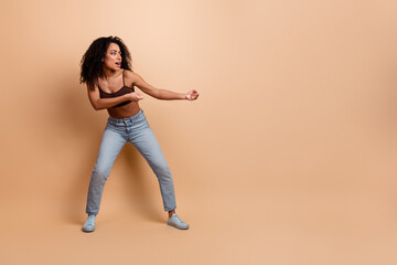 Young female in a casual stylish outfit performing an expressive dance on a beige background, full...