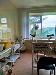 interior of  ginecological office in the hospital. Tiles on the walls and floor, blinds on the window, chair and lamp for examination, tables for instruments and disinfection