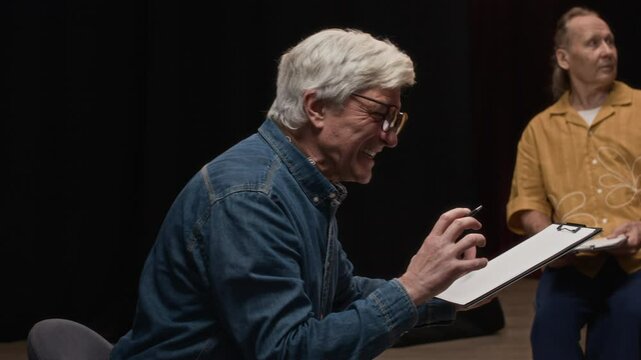 Slowmo shot of senior Caucasian male acting coach holding script directing an improvisation exercise with young African American student during drama class