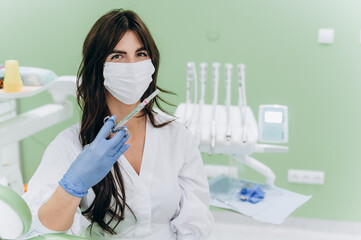 Portrait of a young female dentist wearing mask and holding syringe in modern clinic setting
