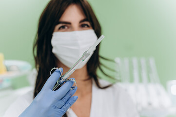 Portrait of a young female dentist wearing mask and holding syringe in modern clinic setting