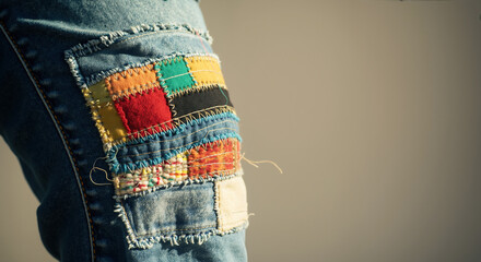 Colorful fabric patches sewn on denim jeans creating artistic patchwork design. Clothing repair and upcycling concept. Fashion alteration services