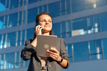 Businesswoman holding digital tablet and talking on phone outdoors on city street