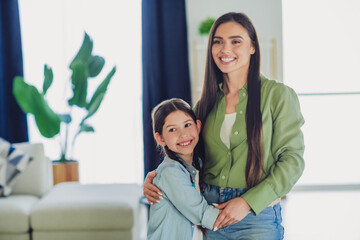 Loving mother and cheerful daughter embracing at home, sharing a happy moment together in a cozy...