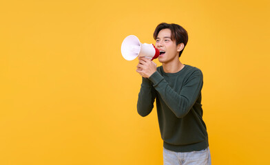 Young Asian man shouting into megaphone making announcement isolated on yellow copy space...