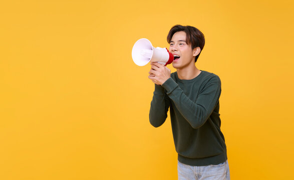 Young Asian man shouting into megaphone making announcement isolated on yellow copy space background.