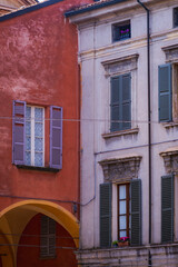 Reggio Emilia, Italy, 01.04.2025.Old European building facades with red wall, grey shutters and arches, urban detail