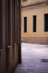 Silent urban alley with yellow facade, iron windows and stone floor in historic European city