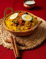 Delicious Indian Biryani Rice Dish with Eggs and Raita Sauce on a Woven Place Mat and Red Background - Authentic Indian Cuisine Photography