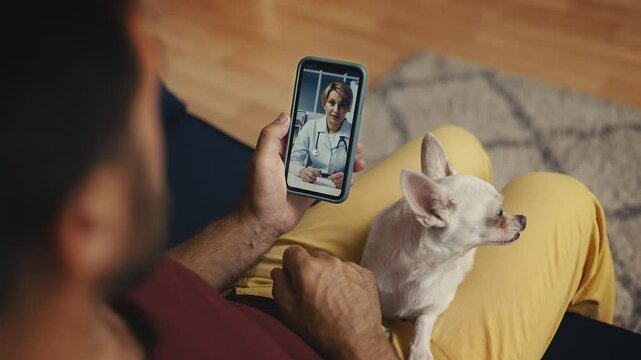 Male owner with dog on lap calling veterinarian, telemedicine consultation