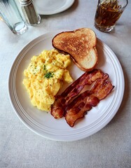 Delicious Breakfast Plate with Scrambled Eggs, Crispy Bacon, Toasted Bread, and a Drink on a Table in a Restaurant Setting