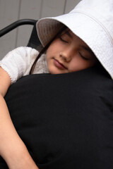 A young girl in a hat peacefully naps, hugging a soft black pillow in a tranquil setting. Perfect for themes of childhood, relaxation, quiet moments, family, dreams, or restful visuals