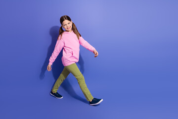 Obraz premium Confident young schoolgirl in vibrant casual attire walking confidently against a colorful violet background for a promotional concept