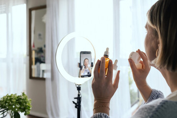 Middle-aged woman beauty blogger filming skincare product unboxing at home with ring light....