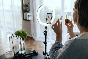 Middle-aged woman beauty blogger filming skincare product unboxing at home with ring light....