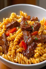  Plato de fusilli con trozos de carne de res, pimientos rojos y salsa espesa, servido caliente.

