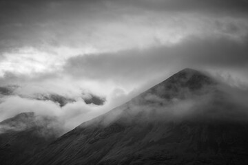 Moody clouds shroud the peaks of mountain ridge and summit on the Isle of Skye in black and white