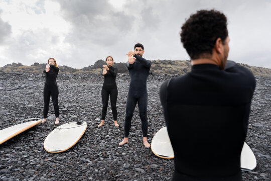 Surfing students stretching with instructor on rocky beach - Powered by Adobe