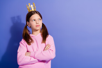 Portrait of a young girl in a pink hoodie wearing a crown with pigtailed hair against a purple...