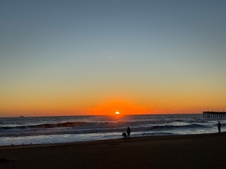 Sunset over the ocean at the beach with silhouettes of people walking along the shore during...