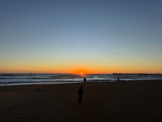 Sunset over the ocean at the beach with silhouettes of people walking along the shore during...