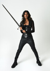 Fantasy female warrior in leather armour  full body studio portrait of fierce brunette in catsuit...