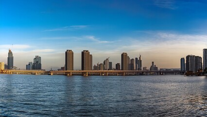 Fototapeta premium Panoramic City Skyline with Skyscrapers, River, Bridge, and Clear Blue Sky at Sunset or Sunrise, Urban Landscape with Modern Architecture