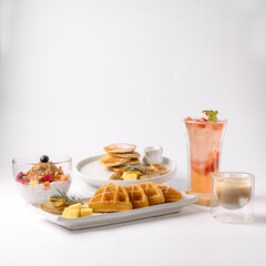 A stylish breakfast spread featuring waffles with butter, pancakes, chia pudding with berries, iced...