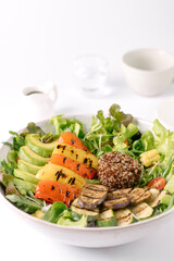 A fresh bowl of salad with grilled vegetables, quinoa, avocado, and leafy greens, presented on a white plate with a minimalist white background.