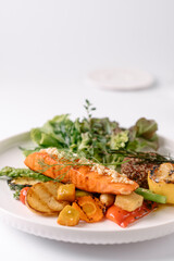 Grilled salmon served with mixed vegetables, quinoa, and fresh greens on a white plate, showcasing a healthy and colorful meal.