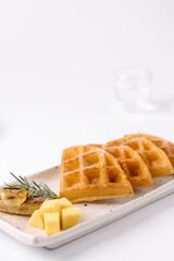 Golden waffles served with butter, cheese cubes, and a rosemary sprig on a white rectangular plate.