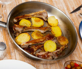 Closeup of spicy fried ribs of lamb with potato on pan over wooden background.