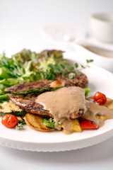 A gourmet steak dish topped with creamy sauce, served with roasted vegetables and fresh greens on a white plate.