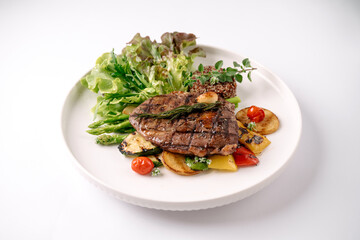 Grilled steak served with fresh asparagus, mixed greens, cherry tomatoes, and roasted vegetables on a white plate.