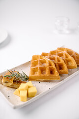 Golden waffles served with cheese cubes and a herb garnish on a rectangular white plate with a minimalist background.