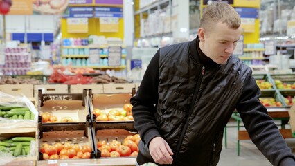 Man choosing vegetables in supermarket, shelves with vegetables. Customer selecting from a variety of fresh vegetables in the supermarket's grocery department while shopping for groceries