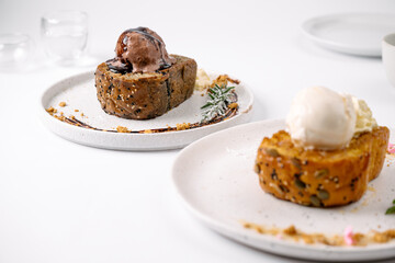 Two plates with bread topped with scoops of chocolate and vanilla ice cream, garnished with herbs, on a white table.