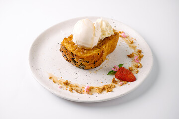 A toasted bun topped with two scoops of vanilla ice cream, garnished with a strawberry, whipped cream, and crumbled nuts on a white plate.