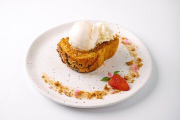 A toasted slice of bread topped with a scoop of vanilla ice cream and whipped cream, garnished with a strawberry half and sprinkled crumbs on a white plate.