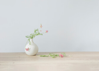 pink wild flowers in round ceramic vase on light wooden table