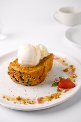 A slice of seeded toast topped with two scoops of vanilla ice cream, garnished with crumbled nuts, edible flowers, and a sliced strawberry on a white plate.