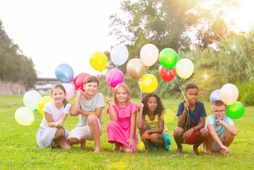 Obraz premium Group photo of happy children playing on lawn with balloons in hands.