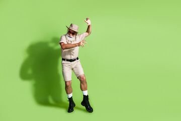Elderly adventurer dancing against green backdrop in safari attire, expressing lively explorer spirit with fashionable safari outfit