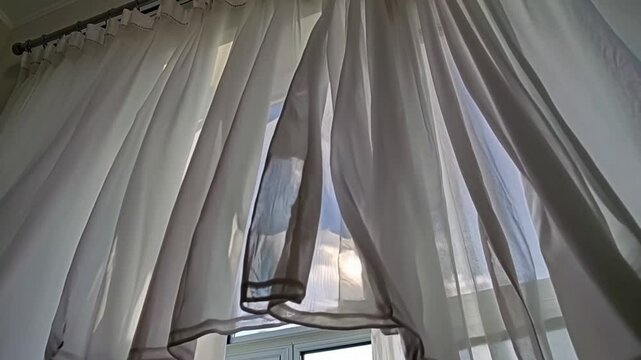 Sheer white curtains gently swaying by the window in sunlight  