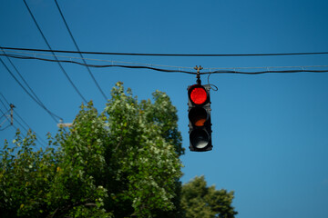 Red Stop Light Against Blue Sky With Power Lines And Trees In The Background